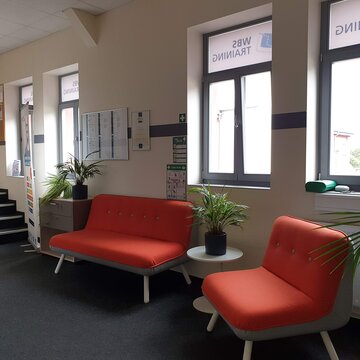 Wartebereich mit zwei roten Sofas und Grünpflanzen.