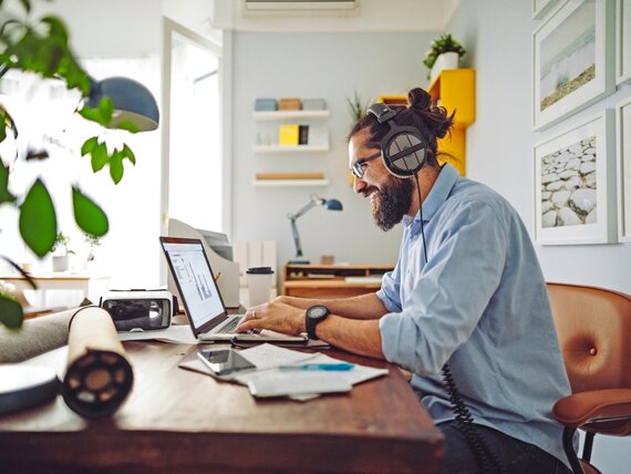 Ein Mann mit Kopfhörern arbeitet im Homeoffice an seinem Laptop.