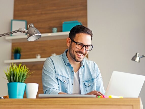 Ein fröhlicher Mann sitzt vor seinem Laptop.