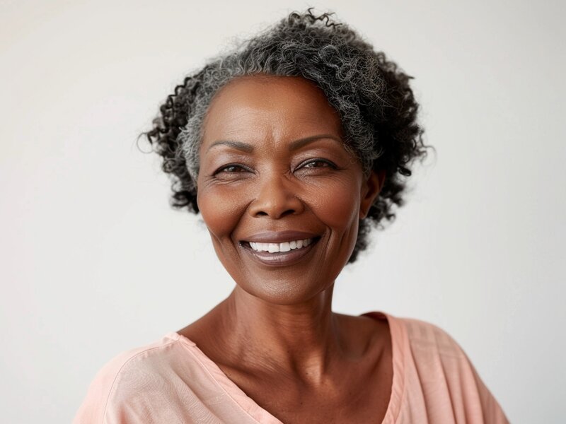 Porträt einer reifen Frau mit kurzen, grauen, gekrausten Haaren, die freundlich lächelt