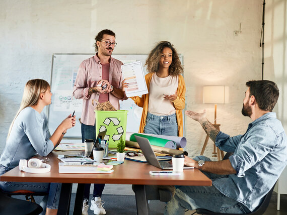 Vier Kolleg:innen besprechen an einem großen Tisch im Büro, wie sie beim Drucken Energie und Papier sparen können.