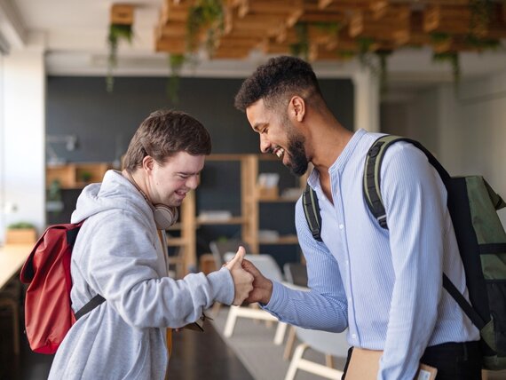 Ein Betreuer und ein Junge mit Behinderung spielen fröhlich Daumendrücken