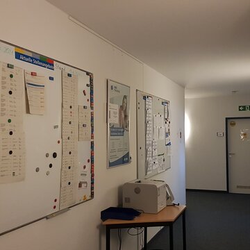 Flur mit 2 Whiteboards auf den Informationszettel hängen. Druckstation mit Papierablage.