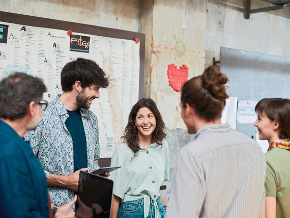 Eine Gruppe Männer und Frauen mit Tablets und Laptops in lockerer Atmosphäre.