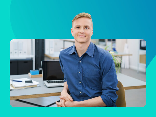 Blonder Mann in blauem Hemd sitzt am Schreibtisch.