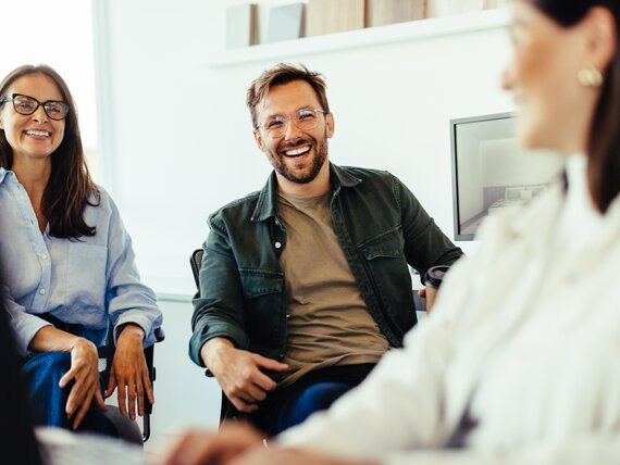 Eine Gruppe fröhlicher Kollegen und Kolleginnen lachen gemeinsam bei der Arbeit