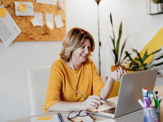 Eine Frau mit Kopfhörern sitzt vor ihrem Laptop und nimmt an einem Videocall teil.