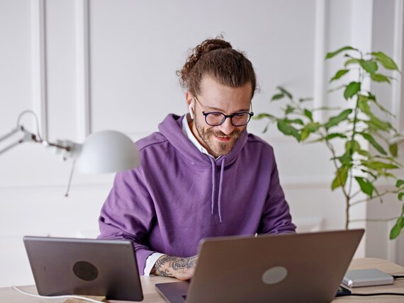 Ein Mann sitzt am Schreibtisch und arbeitet an seinem Laptop und Tablet.