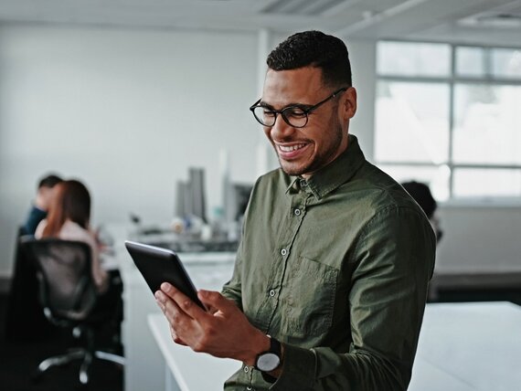 Ein fröhlich lachender Mann im Büro, der auf ein Tablet schaut.