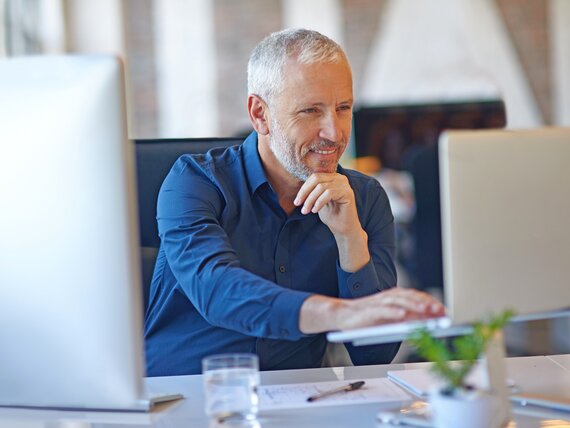 Ein Mann im mittleren Alter arbeitet gut gelaunt an seinem Laptop.