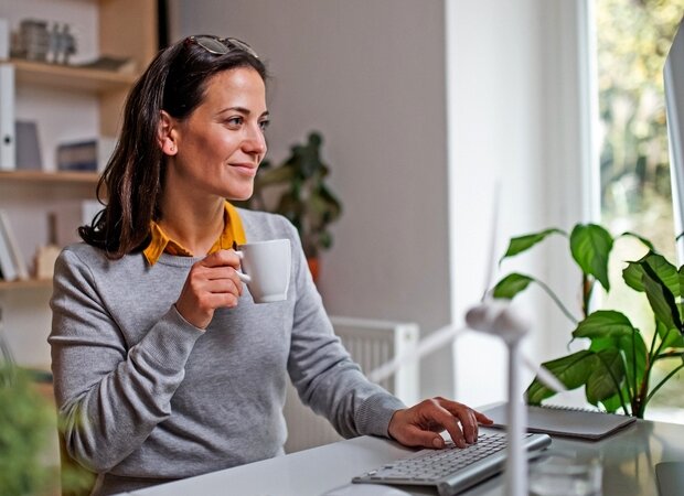 Eine Frau sitzt vor ihrem Computer und hält eine Kaffeetasse in der Hand.