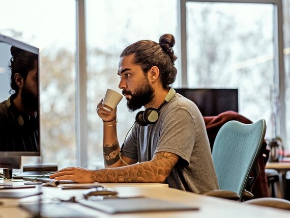 Ein Mann arbeitet am Computer und trinkt einen Kaffee.