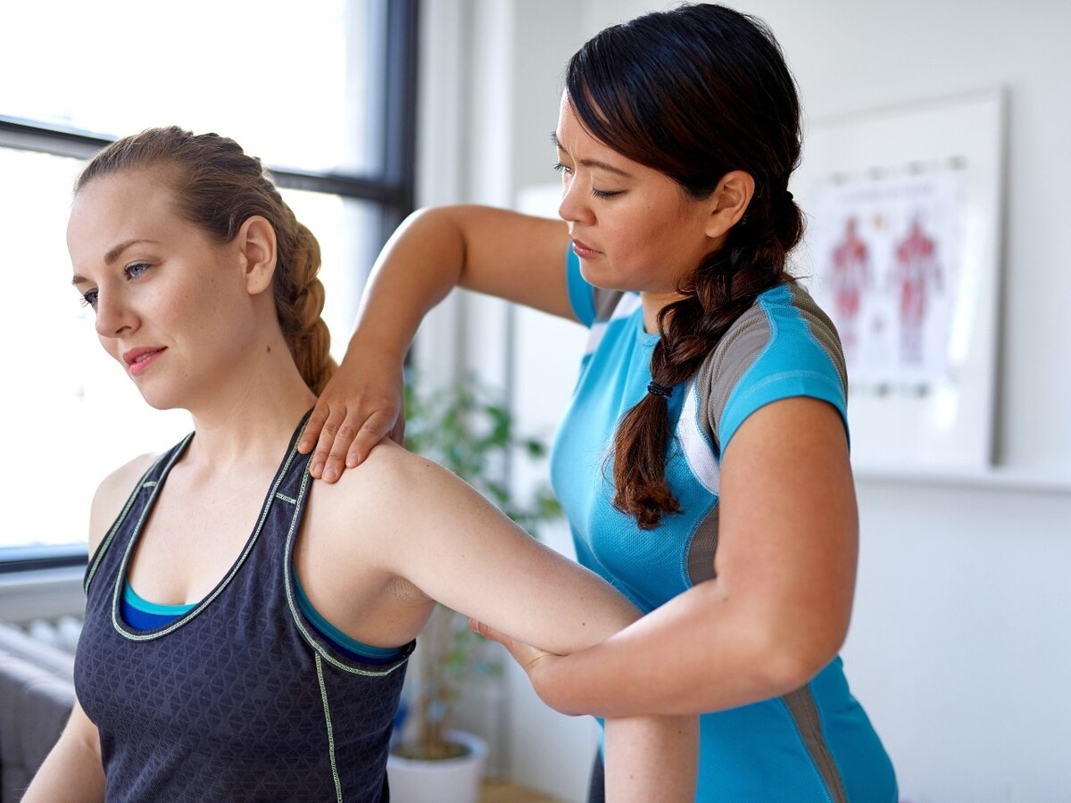 Eine Physiotherapeuten massiert die Schulter einer Patientin