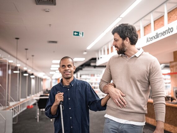 Eine zusätzliche Betreuungskraft begleitet einen blinden Mann.