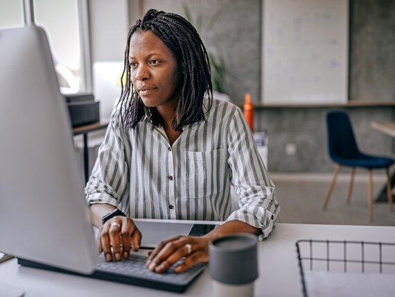 Eine Frau sitzt in einem Büro und liest etwas auf ihrem Computerbildschirm