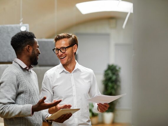 Zwei Männer mit Tablet und Unterlagen in den Händen unterhalten sich locker.