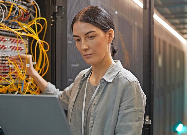 Eine Frau mit Laptop arbeitet an einem Kabelschaltkasten