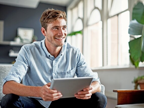 Ein Mann sitzt mit seinem Tablet in den Händen auf einem Sofa.
