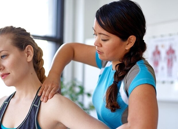 Eine Physiotherapeuten massiert die Schulter einer Patientin