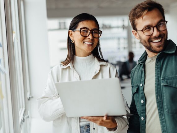 Eine Frau und ein Mann mit Laptop lachen fröhlich.