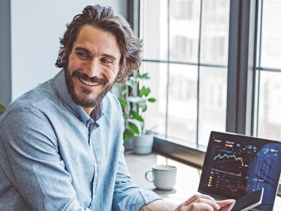 Ein Finanzexperte schaut sich Diagramme und Kurse auf seinem Laptop an und tippt in sein Smartphone