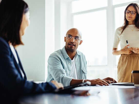 Eine Gruppe junger Kollegen und Kolleginnen befinden sich in einem Meeting und unterhalten sich