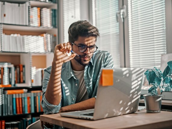 Ein Mann schaut auf seinen Laptop und denkt nach.