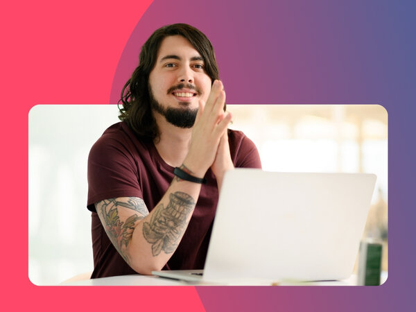 Mann mit langen Haaren und T-Shirt sitzt vor einem Laptop und schaut freundlich