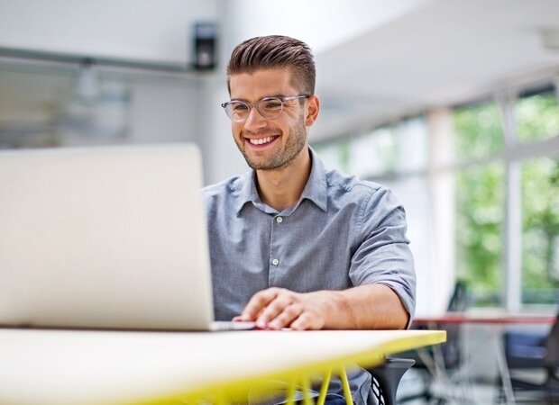 Ein Mann arbeitet fröhlich an seinem Laptop.