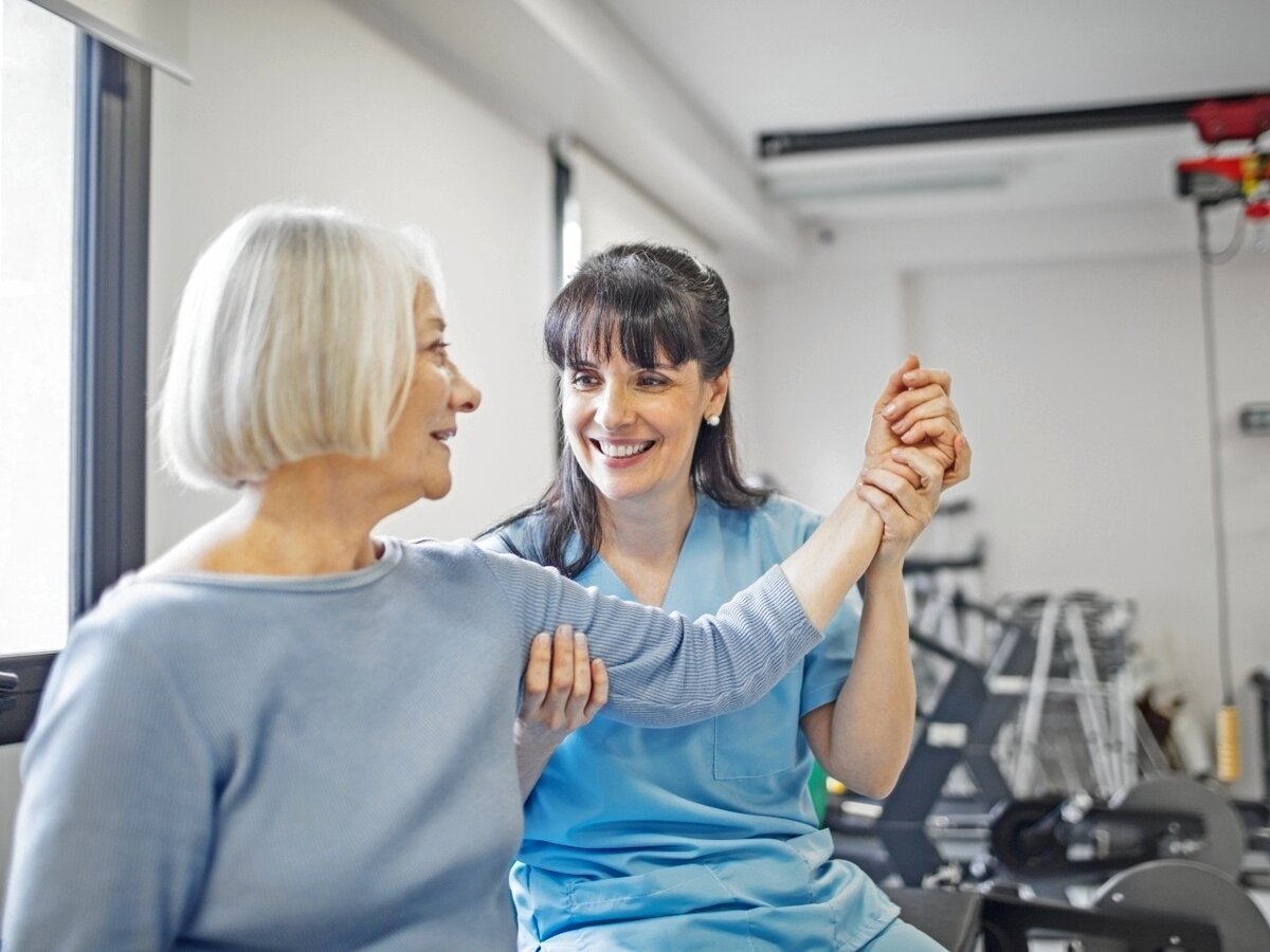 Eine freundliche Physiotherapeutin massiert den Arm einer Seniorin