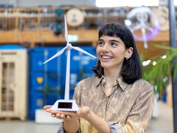 Eine fröhliche Frau schaut sich ein Windrad Modell an, welches sie in den Händen trägt.