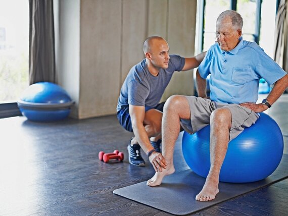 Ein Physiotherapeut macht mit einem Senior Übungen auf einem Gymnastikball