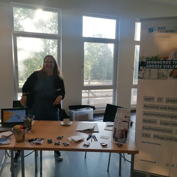 Eine fröhliche Frau steht am Infostand im Jobcenter