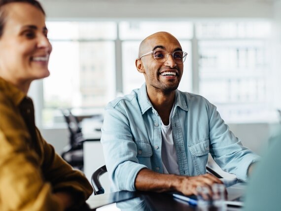 Ein Mann und eine Frau sitzen in einem Büro und lachen fröhlich.