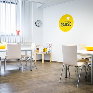 Heller Pausenraum mit weißen Tischen und Stühlen