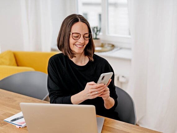 Eine Frau im Homeoffice mit Laptop und Smartphone.
