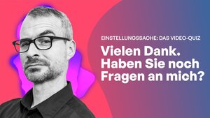 Ein Mann mit schwarzem Hemd und Brille schaut fragend in die Kamera