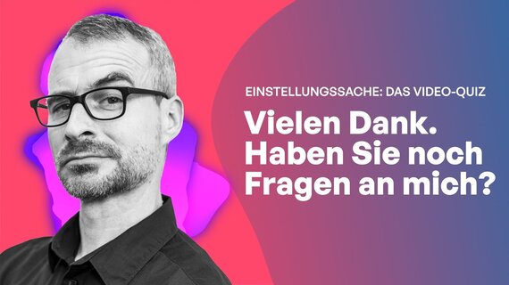 Ein Mann mit schwarzem Hemd und Brille schaut fragend in die Kamera