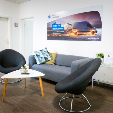 Warteecke mit modernen Sofa und Sessel und Beistelltisch. Rechts steht ein E-Scooter.