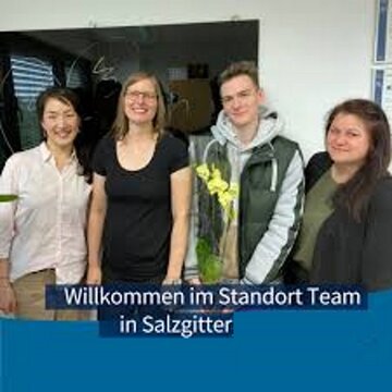 Team aus 4 Personen die freundlich in die Kamera schauen. Ein Kollege hält eine gelbe Orchidee, am unteren Bildrand der Text "Willkommen im Standort Team in Salzgitter"