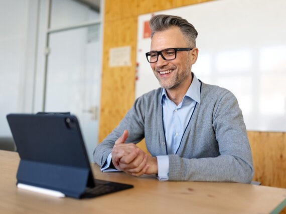 Ein Mann sitzt vor seinem Tablet in einem Konferenzraum und hat einen Videocall