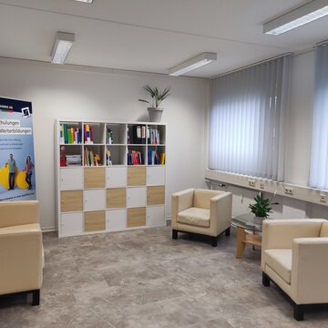 Gemütlicher Pausenraum mit Sessel und Couch und dazu noch ein großes Bücherregal