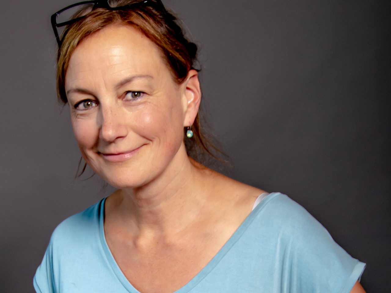 Portrait einer Frau mit Brille auf dem Kopf, die in die Kamera lächelt.